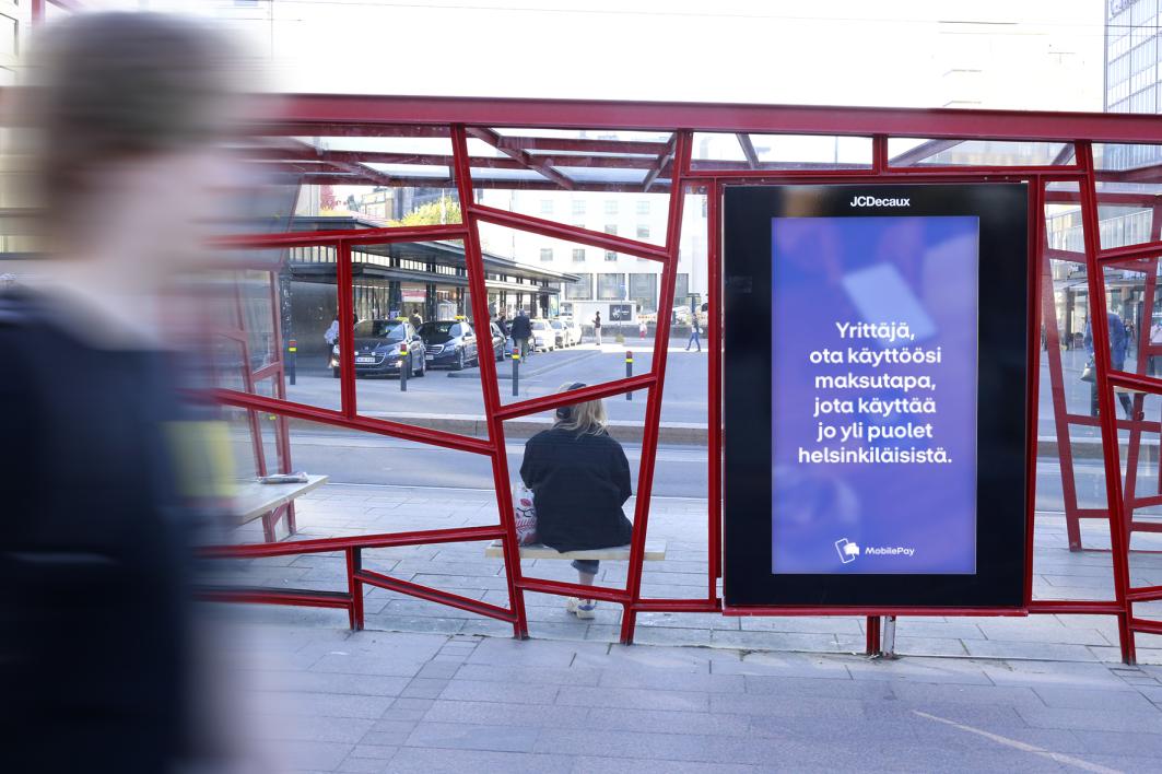 Mobilepayn digitaalinen ulkomainoskampanja Helsingin Tennispalatsin ratikkapysäkillä.